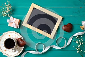 Wedding morning concept. Blank photo frame, heart-shaped chocolate, gift box, ribbon, cup of coffee, daisy flowers. Stylish