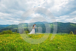 Wedding in mountains, A COUPLE IN LOVE, MOUNTAINS background, STANDING surounded dandelions, AMONG THE LAWN WITH THE GREEN GRASS,