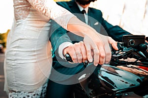 Wedding, newlyweds. A man and a woman in wedding attire hold on to a motorcycle handle, showing off their engagement rings. Hands