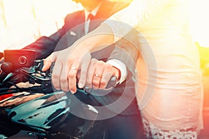 Wedding, newlyweds. A man and a woman in wedding attire hold on to a motorcycle handle, showing off their engagement rings. Hands