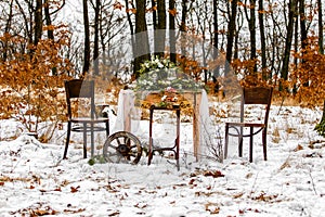 Wedding old wooden table with needlepoint and leaf decoration during wedding ceremony in winter on snow in the middle of forest