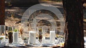 Wedding party banquet outdoors in forest. Dining table decorated in boho style with candles, white cloth, flowers
