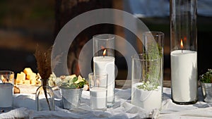 Wedding party banquet outdoors in forest. Dining table decorated in boho style with candles, white cloth, flowers