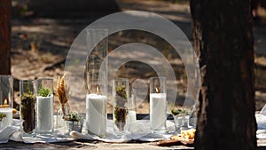 Wedding party banquet outdoors in forest. Dining table decorated in boho style with candles, white cloth, flowers