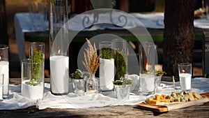 Wedding party banquet outdoors in forest. Dining table decorated in boho style with candles, white cloth, flowers