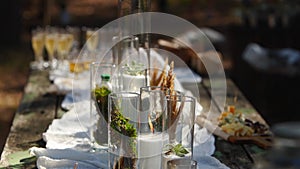 Wedding party banquet outdoors in forest. Dining table decorated in boho style with candles, white cloth, flowers