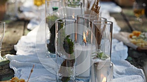 Wedding party banquet outdoors in forest. Dining table decorated in boho style with candles, white cloth, flowers