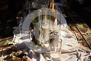 Wedding party banquet outdoors in forest. Dining table decorated in boho style with candles, white cloth, flowers