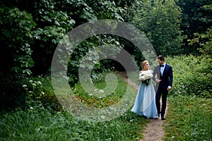 Wedding photo shoot and walk. The groom and the bride, the bride`s blue dress, and a bouquet of peonies. In the Park, on