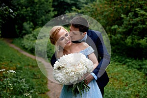 Wedding photo shoot and walk. The groom and the bride, the bride`s blue dress, and a bouquet of peonies. In the Park, on