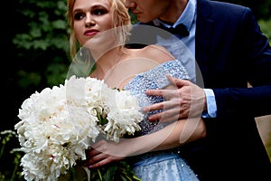 Wedding photo shoot and walk. The groom and the bride, the bride`s blue dress, and a bouquet of peonies. In the Park, on