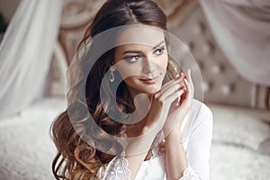 Wedding Portrait of Beautiful Bride girl smiling. Brunette with makeup and long curly hair style wearing in white sexy boudoir