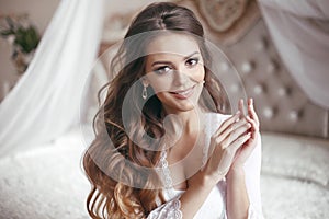 Wedding Portrait of Beautiful Bride girl smiling. Brunette with makeup and long curly hair style wearing in white sexy boudoir