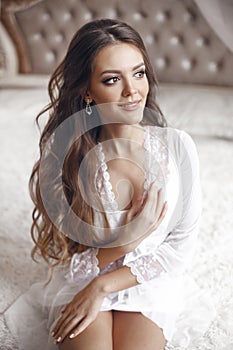 Wedding Portrait of Beautiful Bride girl smiling. Brunette with makeup and long curly hair style wearing in white sexy boudoir