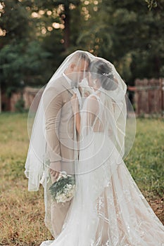 Wedding portrait of the bride and groom. Happy bride and groom gently hug each other under the veil, pose and kiss.