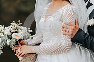 Wedding portrait. A brunette bride in a long dress and a groom in a classic suit pose under a veil