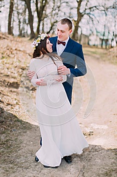 Wedding portrait of happy stylish newlywed bride and groom posing outdoor with leafless trees at background