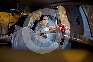 Wedding portrait. Happy young stylishly dressed couple is sitting in the car and looking through window. The bride with