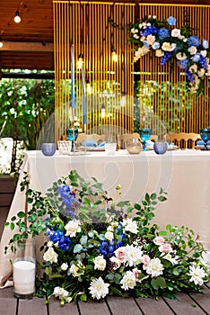 Wedding presidium, banquet table for newlyweds with flowers, greenery, blue and gold color. Lush flower arrangement on the wedding