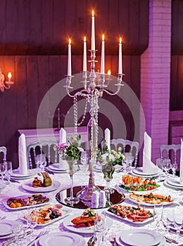 Wedding reception dinner. Round table served with flowers, shiny candles and appetizer food. Holiday banquet menu