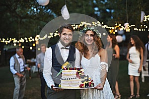 Bride and groom holding a cake at wedding reception outside in the backyard.