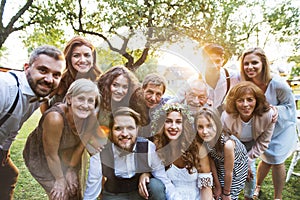 Bride, groom, guests posing for the photo at wedding reception outside in the backyard.