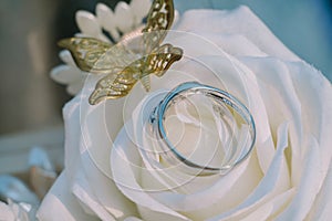 A wedding ring adorned with a delicate white rose and butterfly motif crafted from gold,