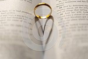 A wedding Ring on the bible with shadow of heart shape on the page