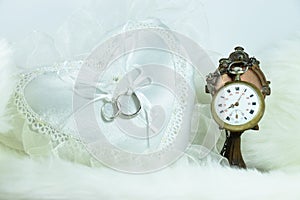 Wedding ring on heart pillow, clock on soft fabric