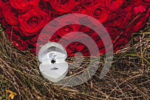 Wedding ring in a white box with a bouquet of red roses