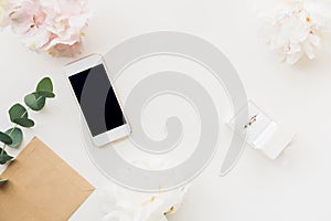 Wedding ring in white gift box on background of flowers and phone. top view