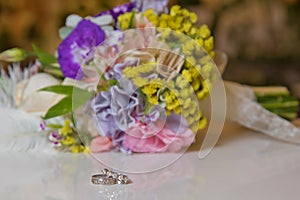 Beautiful toned picture with Engagement rings lie on a wooden surface against the background of a bouquet of flowers . wedding