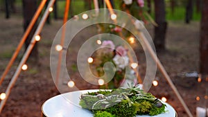 Wedding rings bedding of grass and moss on white table next to bohemian tipi arch decorated in boho style with flowers