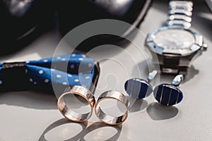 Wedding rings. Black leather shoes, watch, blue bow tie and cufflinks, on a white window sill.