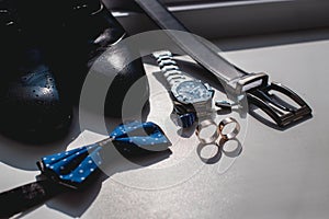 Wedding rings. Black leather shoes, watch, blue bow tie and cufflinks, on a white window sill.