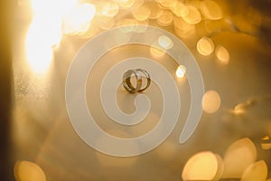 Wedding rings on blured bokeh glowing golden background. Symbol of love and romance on a textured glitter background