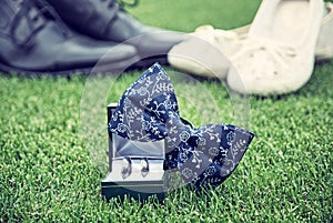 Wedding rings, bow tie and women`s and men`s shoes on grass