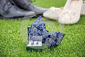 Wedding rings, bow tie and women`s and men`s shoes on the green