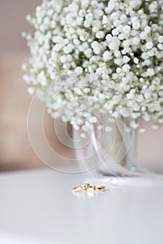 Wedding rings and a bridal bouquet over a white table