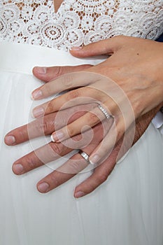 Wedding rings on bride groom hands on white dress background