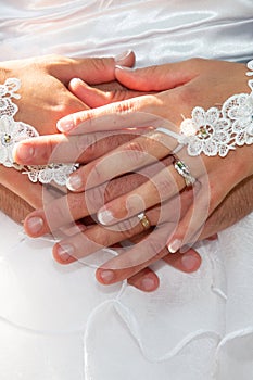 Wedding rings fingers on bride groom hands on white dress background
