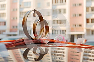 Wedding rings, flowers and ribbon on the roof of the car on the background of city buildings