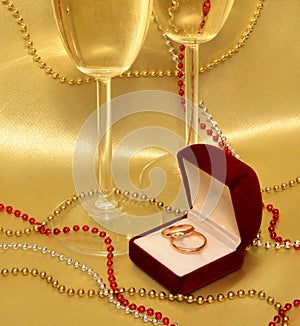 Wedding rings and glasses with sparkling wine on a golden background