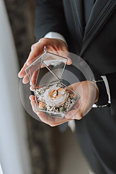 wedding rings in the hands of an adult man decorated in a glass box