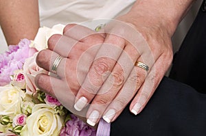 Wedding rings, hands and bouquet of roses.