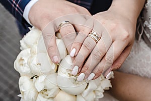 Wedding rings on hands of a newlywed on a background of a bride`s bouquet