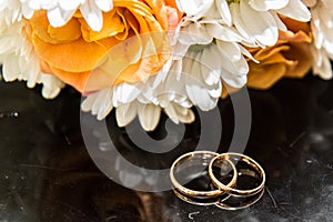 Wedding rings lie on a bouquet of orange roses and white colors.