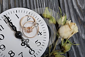 Wedding rings lie on the dial of the watch. Nearby dried roses. On brushed pine boards painted in black and white