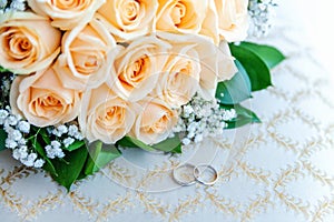 Wedding rings lie on light surface against background of bouquet of flowers