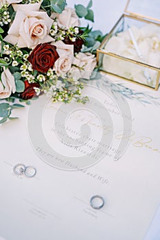 Wedding rings lie on the marriage certificate on the table near the bouquet of flowers